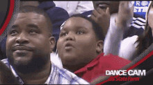 a man and a boy are watching a basketball game with the words dance cam state farm on the bottom right