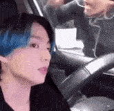 a man with blue hair is sitting in the driver 's seat of a car with another man .