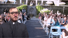 a man with glasses is standing in front of a crowd at a wedding