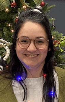 a woman wearing glasses is standing in front of a christmas tree .