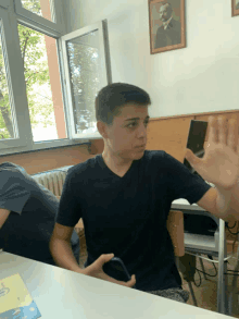 a boy in a black shirt is sitting at a desk with his hand out