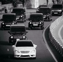 a black and white photo of a group of cars driving down a road .