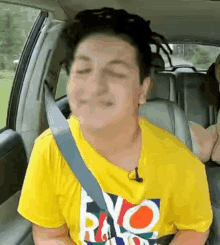 a young man is sitting in the back seat of a car wearing a yellow shirt and a seat belt .