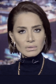 a close up of a woman 's face wearing a black turtleneck and earrings .