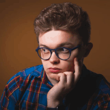 a young man wearing glasses and a plaid shirt is thinking