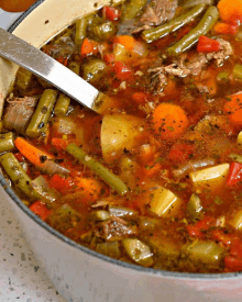 a pot of soup with green beans carrots and potatoes with a spoon in it