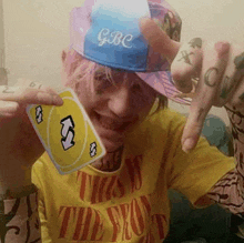 a person wearing a yellow shirt and a blue hat is holding a uno card .