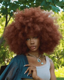 a woman with a large afro wearing a white tank top and a necklace