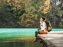 a woman with a backpack sits on a wooden dock overlooking a lake