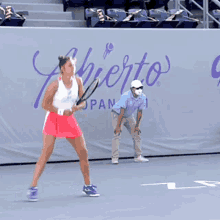 a woman in a pink skirt is holding a tennis racquet in front of a wall that says " guadalajara "