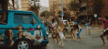 a group of people are dancing in front of a blue van that has a picture of a woman on it