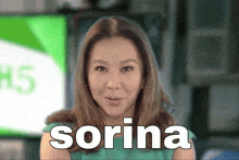 a woman is standing in front of a green screen with the name sorina on it .