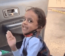 a little girl wearing a headset is sitting in the back of a car and waving .