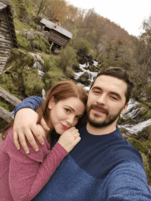 a man and a woman are posing for a picture in front of a waterfall