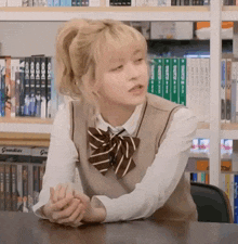 a girl in a school uniform is sitting at a table in front of a bookshelf in a library .