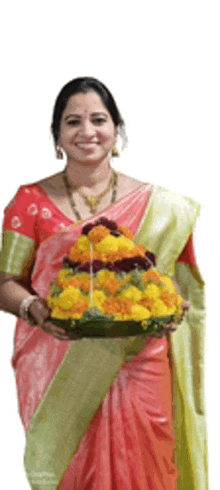 a woman in a pink and green sari is holding a tray of flowers