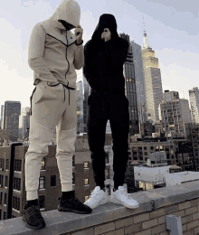 two men are standing on a ledge with a city in the background