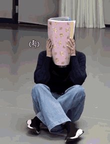 a woman sits on the floor covering her face with a pink book that says ' korean ' on it