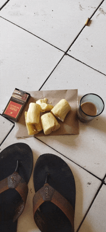 a pack of lucky strike cigarettes sits on a tiled floor next to a banana and a cup of coffee