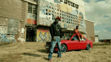 a man standing next to a red car in front of a building that has the word ethu on it