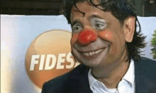 a man is wearing a clown 's nose and smiling in front of a sign that says fides .