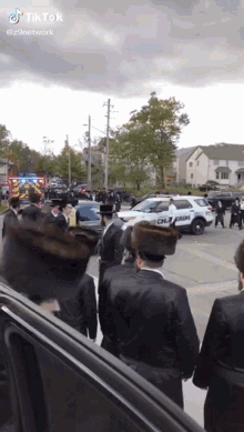 a group of men are walking down a street in front of a police car that says police on it