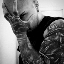 a man with a skull tattoo on his hand is covering his face with his hand