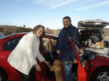 a man and a woman are getting out of a red car