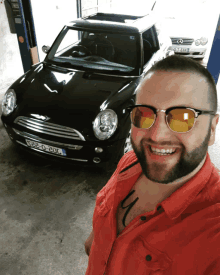 a man wearing sunglasses stands in front of a black mini cooper with a license plate that says nf2c0-20l