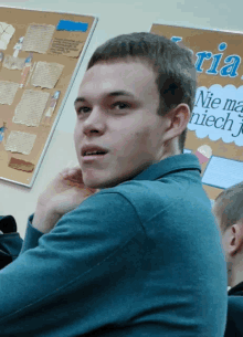 a young man sits in front of a bulletin board that says nie ma niech j