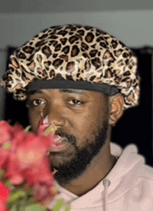 a man with a beard wearing a leopard print hat smells a flower