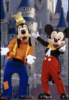 goofy and mickey mouse are posing for a picture in front of a castle