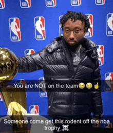 a man in a black jacket holds a trophy in front of a nba backdrop