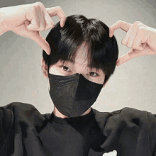 a person wearing a black face mask making a heart with their hands