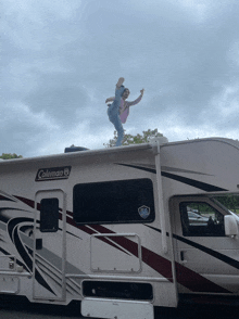 a woman stands on the roof of a coleman camper