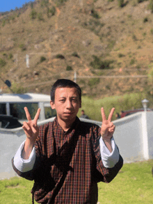 a young man in a plaid shirt is giving a peace sign