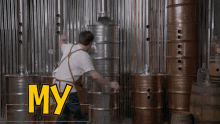 a man in an apron is standing in front of a stack of metal barrels with the word my written in yellow