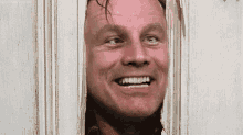 a man is smiling while looking through a door .