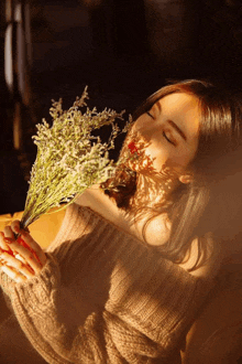 a woman in a sweater is holding a bouquet of flowers in front of her face