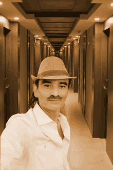 a man taking a selfie in a hallway wearing a hat and a white shirt