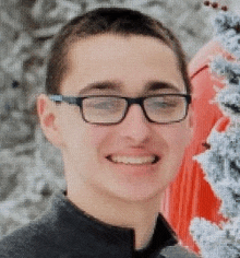 a young man wearing glasses is smiling and standing in front of a christmas tree .