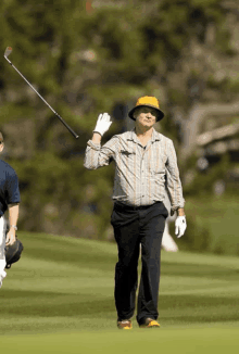 a man wearing a yellow hat and white gloves is holding a golf club