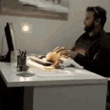 a man sitting at a desk with a cat laying on top of him