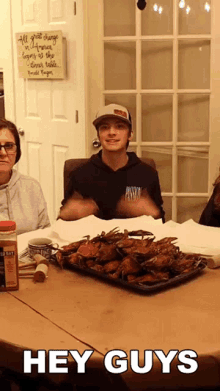 a man sitting at a table with a tray of crabs and a sign that says " hey guys "