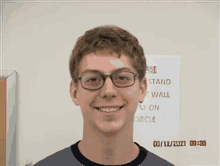 a young man wearing glasses is smiling in front of a sign that says " case stand "