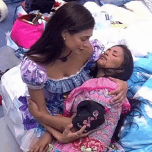 two women are hugging each other on a bed . one of the women is holding a baseball cap .