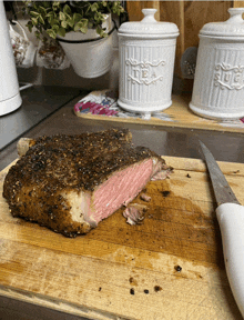 a piece of meat is being sliced on a cutting board in front of a tea and sugar canister