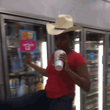 a woman wearing a cowboy hat holds a cup in front of a refrigerator with a sign that says $ 13