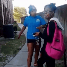 two women standing on a sidewalk one wearing a blue shirt that says ' i am a nurse ' on it