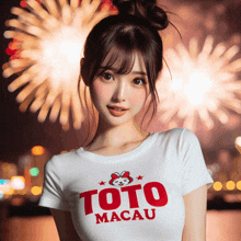 a woman wearing a toto macau shirt stands in front of a fireworks display